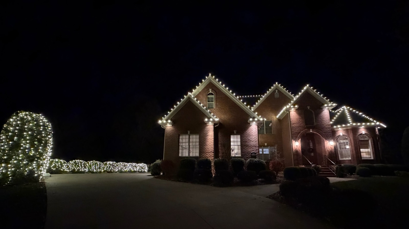 Grand two-story brick home with lit columns, glowing hedges, and full roofline holiday lighting at night in Bowling Green KY