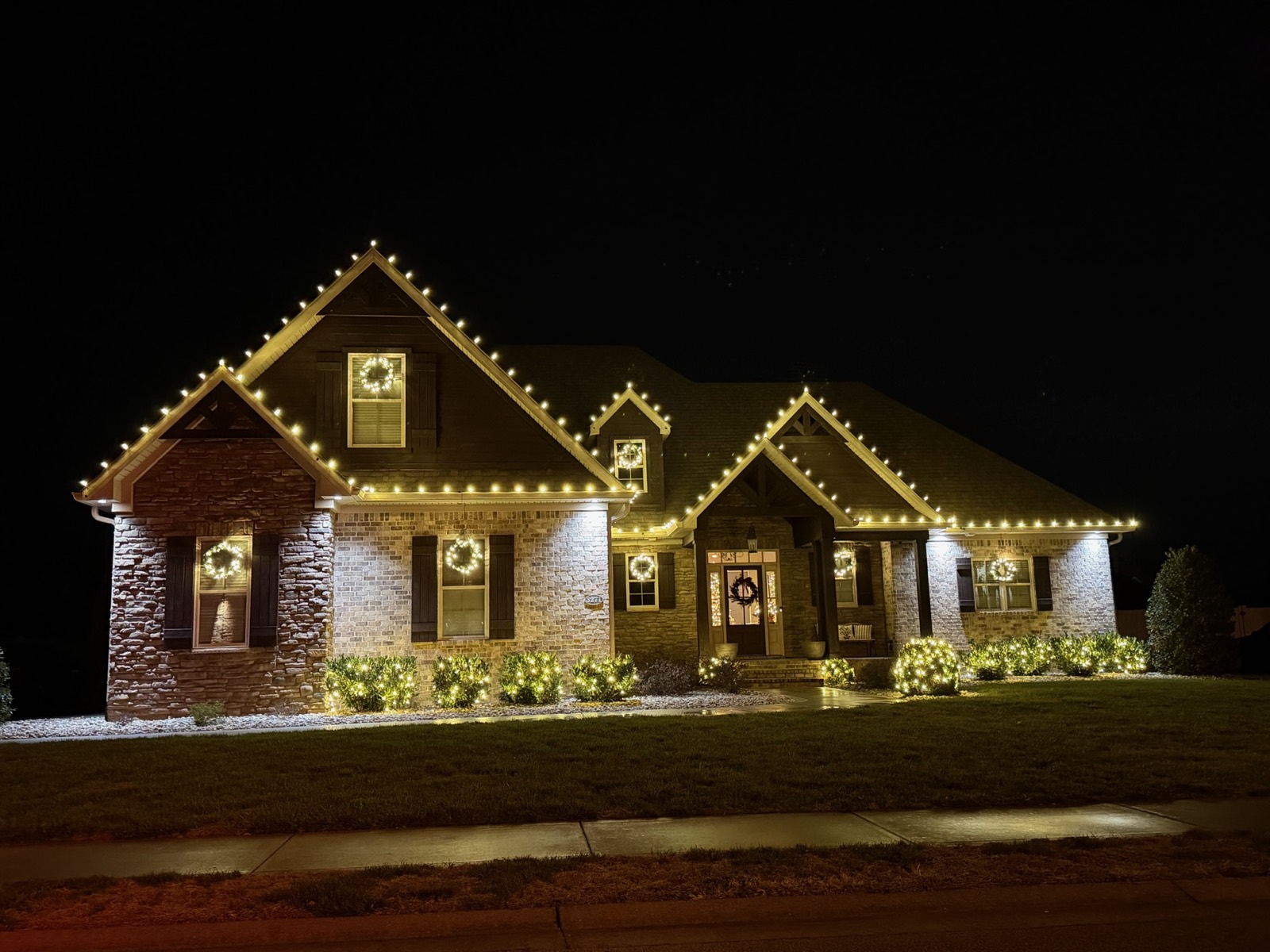 Brick two-story home with warm white roofline lighting and wreaths in every window, Bowling Green KY