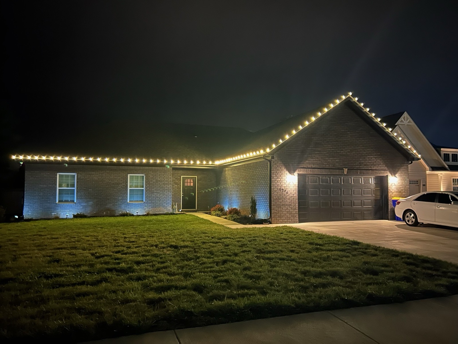 Ranch home with warm white roofline holiday lighting across the full elevation